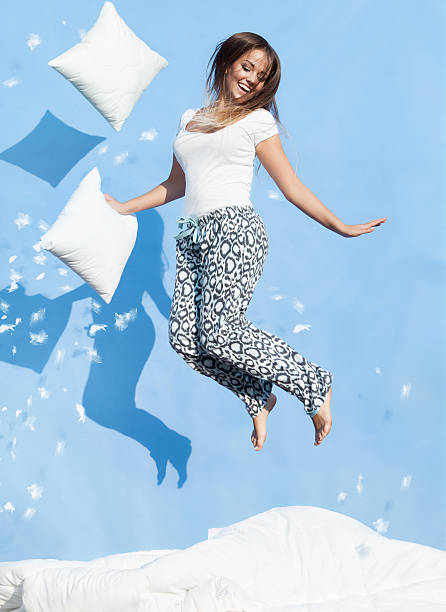 istock Young woman holding a pillow jumping up on bed 483604512