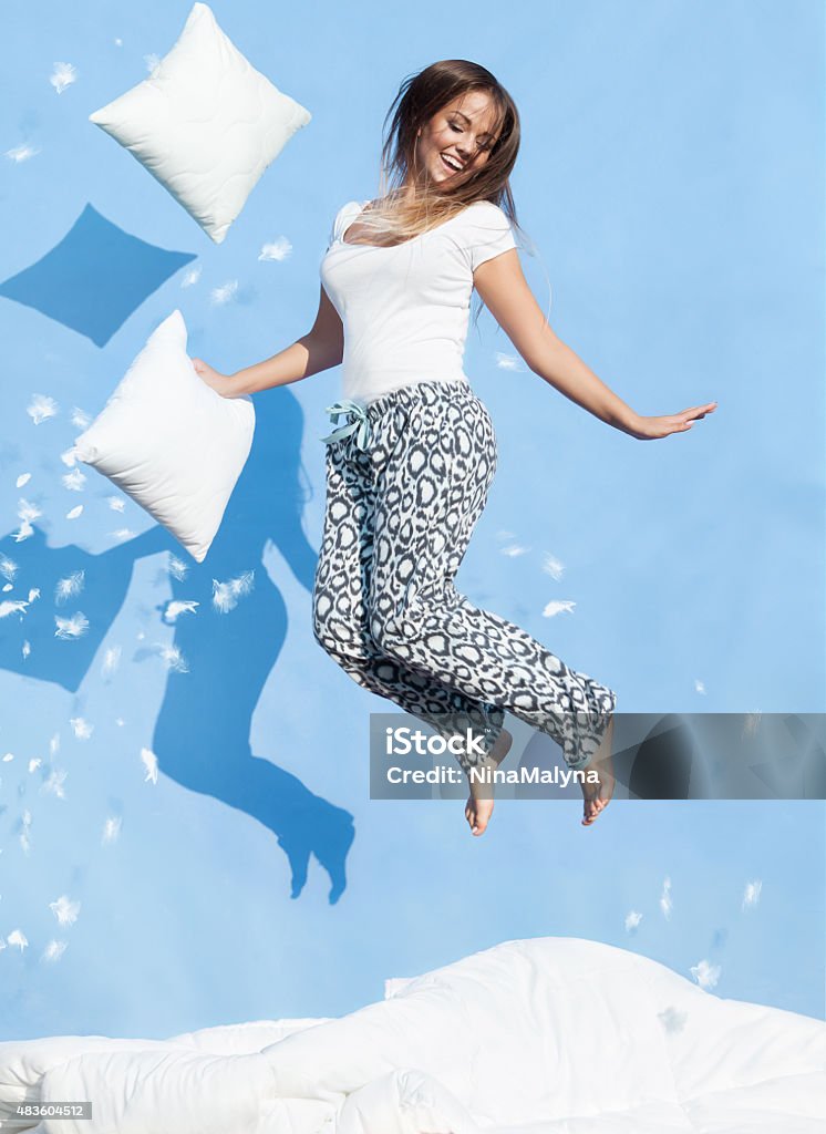 Young woman holding a pillow jumping up on bed Happy morning concept, woman holding a pillow jumping up on bed Bed - Furniture Stock Photo