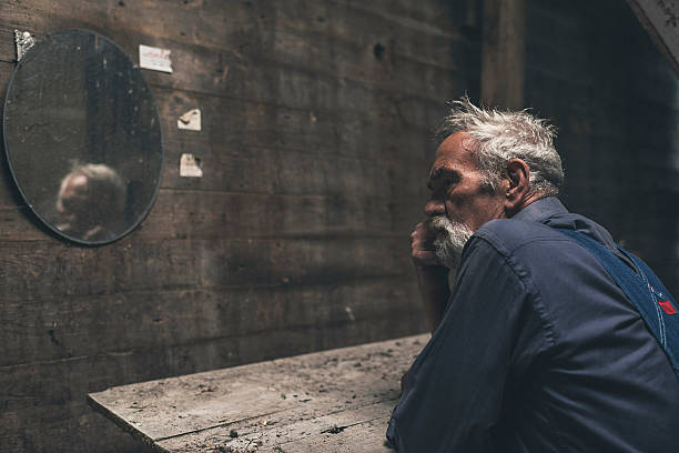 Thoughtful Senior Bearded Man Sitting Inside the Farmhouse, Looking Into the Distance Seriously.