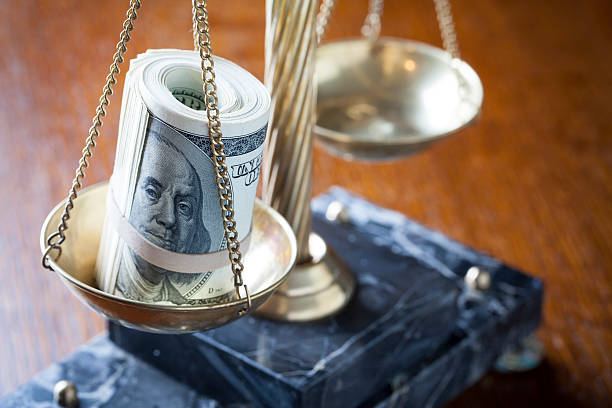 Scales of Justice on wood table with roll of money on pan