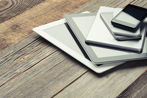 Stack of mobile devices on a wooden table. There are smart phones, digital tablets and mini digital tablets and phablets. 6 devices in all. All screens are blank. The wood is distressed an old. High angle view with copy space