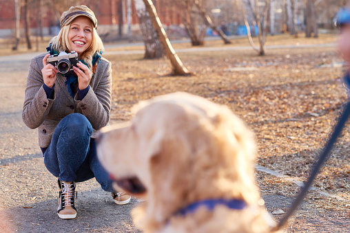 Smiling young woman holding photographic equipment and preparing to take photo of dog