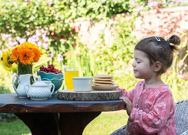 Photo of Toddler girl having breakfast in the garden