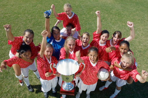 Group of excited multiethnic female soccer team holding trophy on field