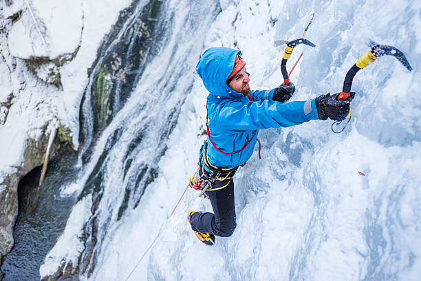 Adult man ice climbing a frozen cascade Brave climber facing an extreme ice terrain axe photos stock pictures, royalty-free photos & images