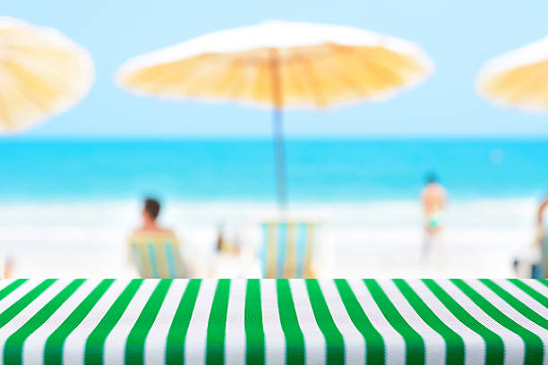 istock Table covered with green striped tablecloth on blurred beach background 483631380