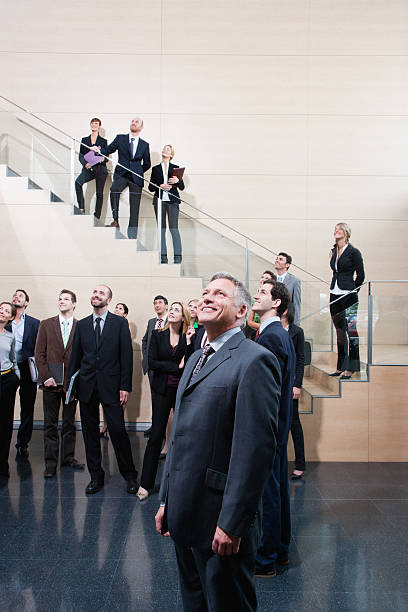 businesspeople looking up in office lobby - onconventioneel leiderschap stockfoto's en -beelden