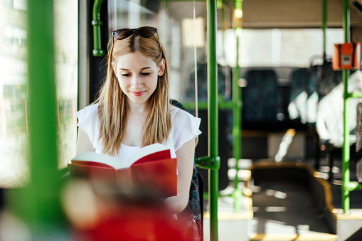 Blonde student girl is reading a book while commuting