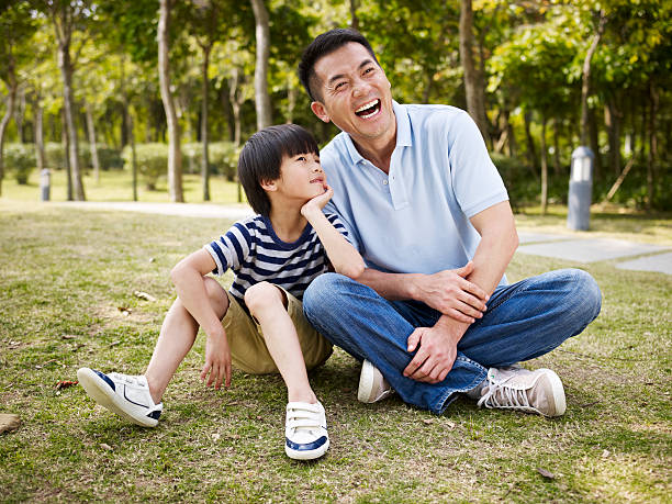 asian father and son having a conversation asian father and elementary-age son sitting on grass outdoors having an interesting conversation. child japanese culture japan asian ethnicity stock pictures, royalty-free photos & images