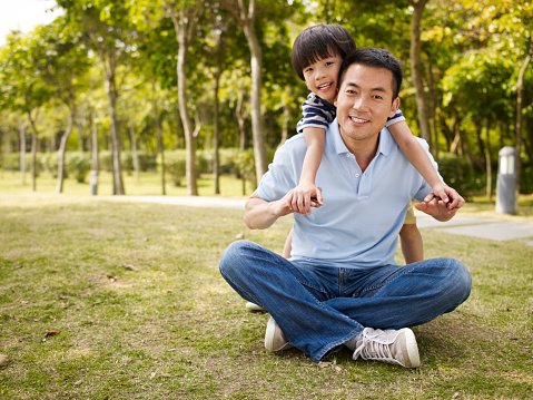 asian father and elementary-age son enjoying outdoor activity in park.