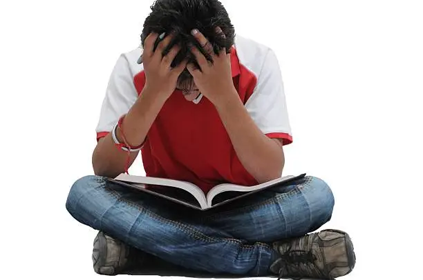 Depressed Indian boy sitting on floor & holding his head. Frustrated with exam pressure.
