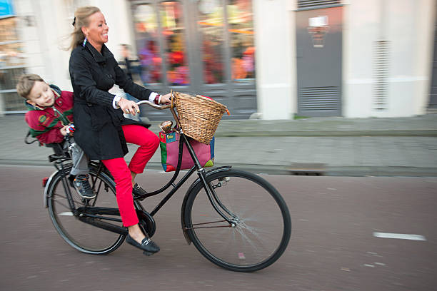 Amsterdam, Netherlands, The - March 9, 2014: A young beautiful mother and her baby riding a bicycle in Amsterdam city.
