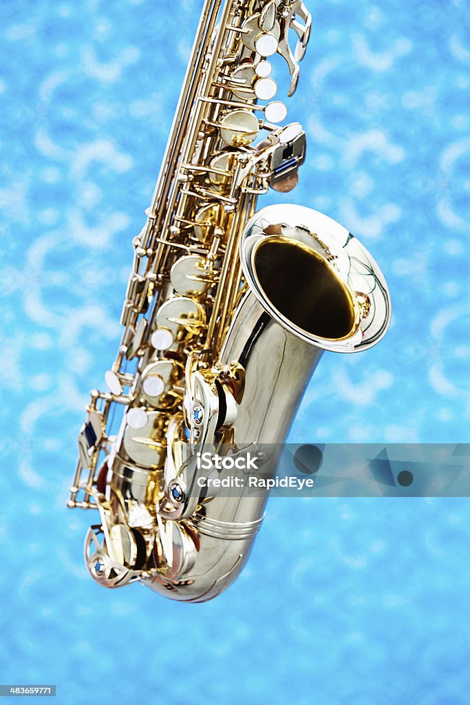 Cropped look at bell and keys of saxophone against blue Cropped shot of  a shiny alto saxophone against  out-of-focus, blue-patterned background. American Culture Stock Photo