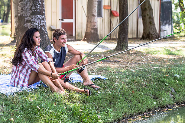 Young couple fishing at lake Young couple fishing at lake sitting on plaid funny camping signs pictures stock pictures, royalty-free photos & images