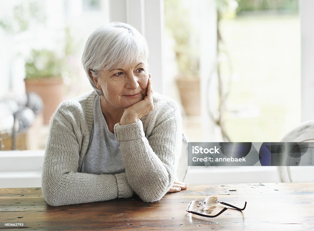 Lost in pleasant memories A senior woman sitting at her kitchen table lost in thought Widow Stock Photo