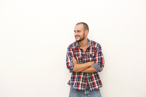 Smiling young man in plaid shirt standing with arms crossed against white background