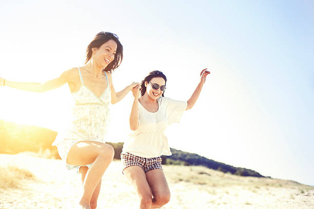 Two beautiful women running on the beach. They running and jumping and expressing positivity. One of the women is wearing sunglasses