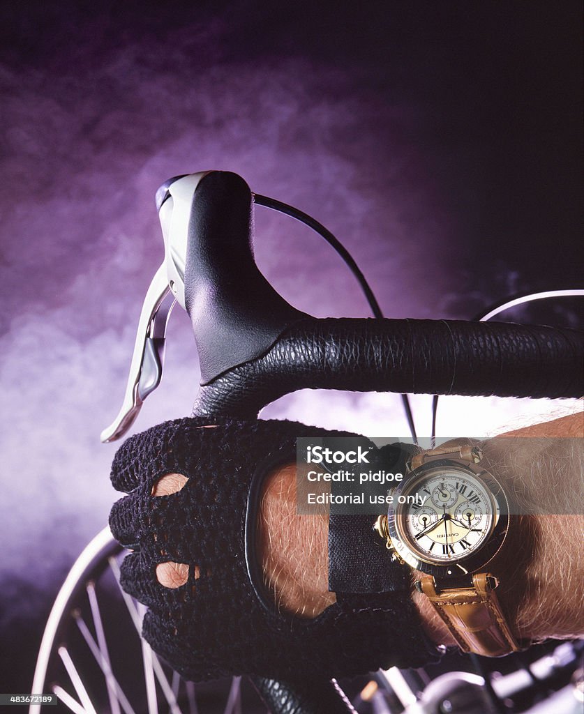 Bicycle  time Amsterdam, the Netherlands - March 31, 2014: close up on handlebar with hand of a cyclist with cycling glove and Cartier Calibre Chronograph Watch on dark and smoky background, selective focus on foreground Cartier Stock Photo