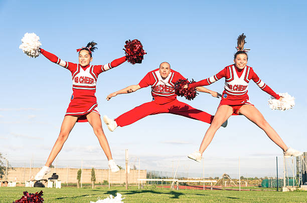 Cheerleaders team with male Coach performing a synchronized jump Cheerleaders team with male Coach performing a synchronized jump cheerleader photos stock pictures, royalty-free photos & images