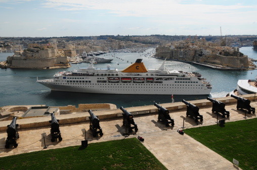 Valletta, Maltese Islands  - October 25, 2013: The Costa Voyager cruise liner part of the Costa Crociere fleet, leaving Valletta and The Grand Harbour with passengers on the upper decks enjoying views of the Upper Barrakka Gardens and The Three Cities.