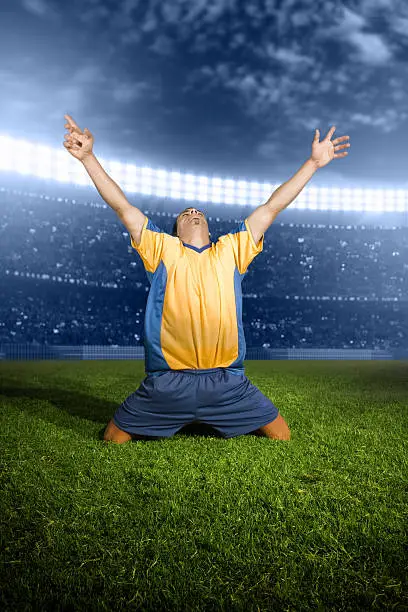 Soccer player slides on his knees with outstretched arms after a goal. Vertical shot.