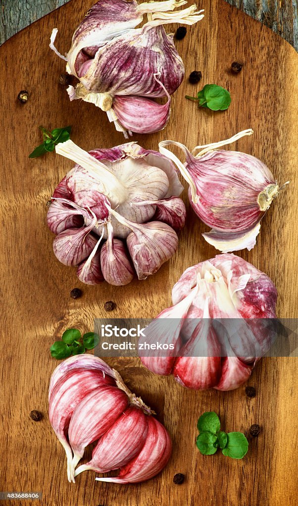 Pink Garlic Raw Pink Garlic Full Body with Greens and Black Peppercorn closeup on Cutting Board. Top View 2015 Stock Photo