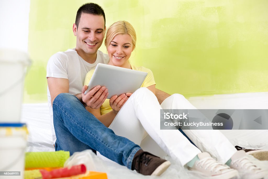 couple using tablet while painting home Young couple using tablet and choosing idea for painting  their home Adult Stock Photo