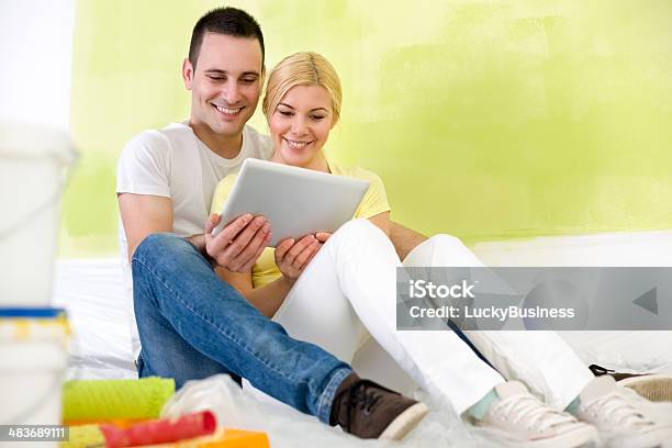 Couple Using Tablet While Painting Home Stock Photo - Download Image Now - Adult, Apartment, Cheerful