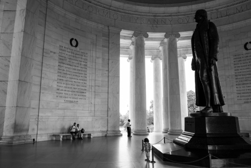 Washington DC, USA - August 18, 2008: A young girl explores in front of a statue of Thomas Jefferson inside the Jefferson Memorial in Washington DC. Two adult visitors and a security guard are also inside the memorial.