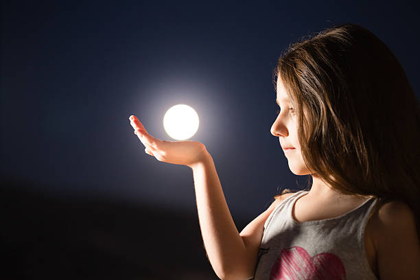 Young girl holding the moon in her hand.