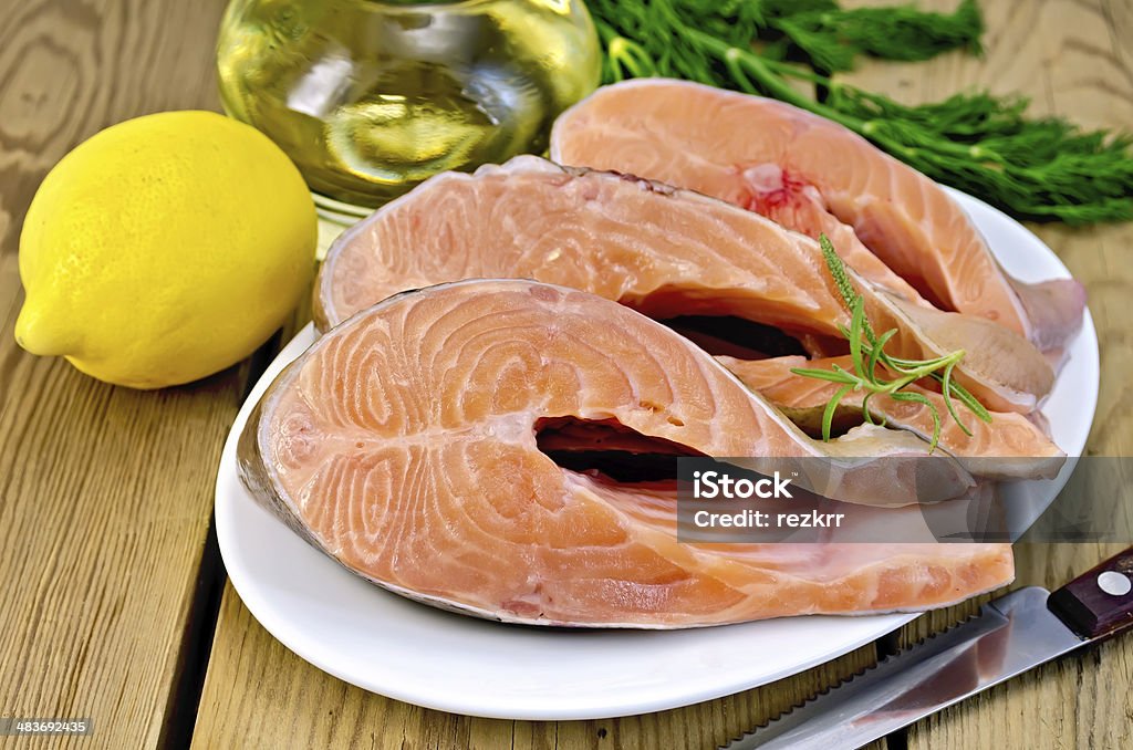 Trout in plate with lemon on board Three pieces of trout in white plate with rosemary, lemon, vegetable oil, dill on a wooden boards background Backgrounds Stock Photo