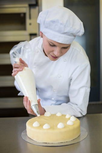 Female baker or confectioner prepares cake with whipped cream