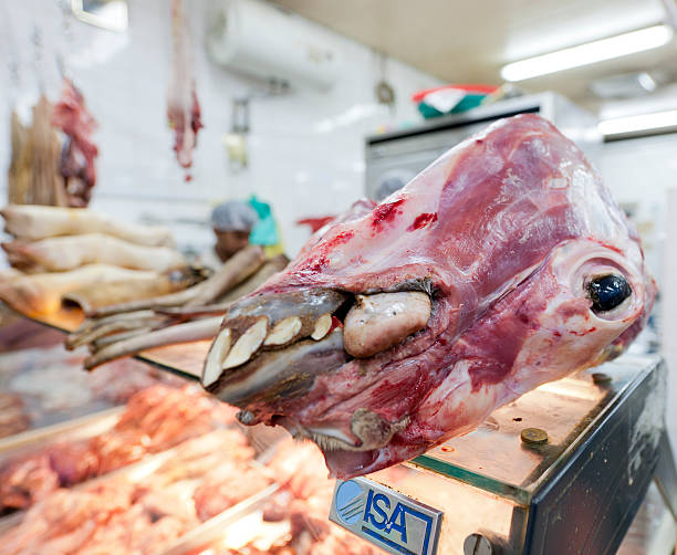 A vivid display of fresh meat cuts, including a pig head, inside a transparent showcase at a vibrant market scene. The arrangement, with visible details of traditional butchery, depicts the authenticity of local market practices and offers insights into cultural culinary traditions.