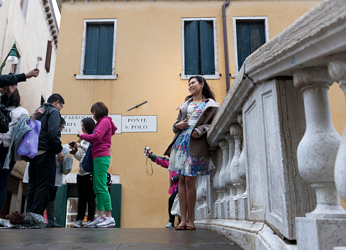Venice, Italy - May 16, 2013: Japanese woman is being photographed with a smart phone on the Ponto s. Polo in Venice. In the background other japanese tourist looking at their cameras 