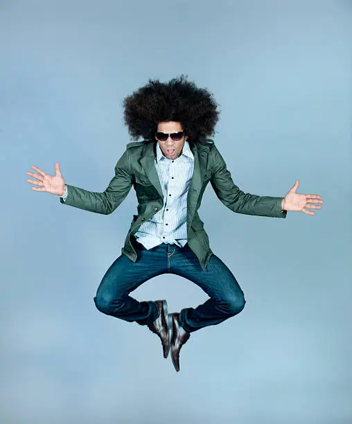 Agile hip hop dancer with an afro hairstyle and cool sunglasses jumping high into the air as he performs for his audience