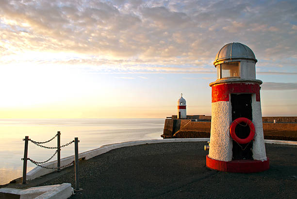 Lighthouses on breakwater wall with calm sea during sunrise.  Tranquil scene on Isle of Man