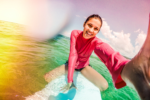 Smiling surfer girl is making a selfie, while being on the surfboard