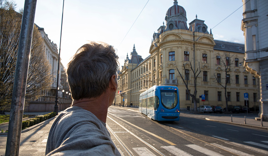 Man looks down urban road to approaching cablecar, selfie, Zagreb, Croatia