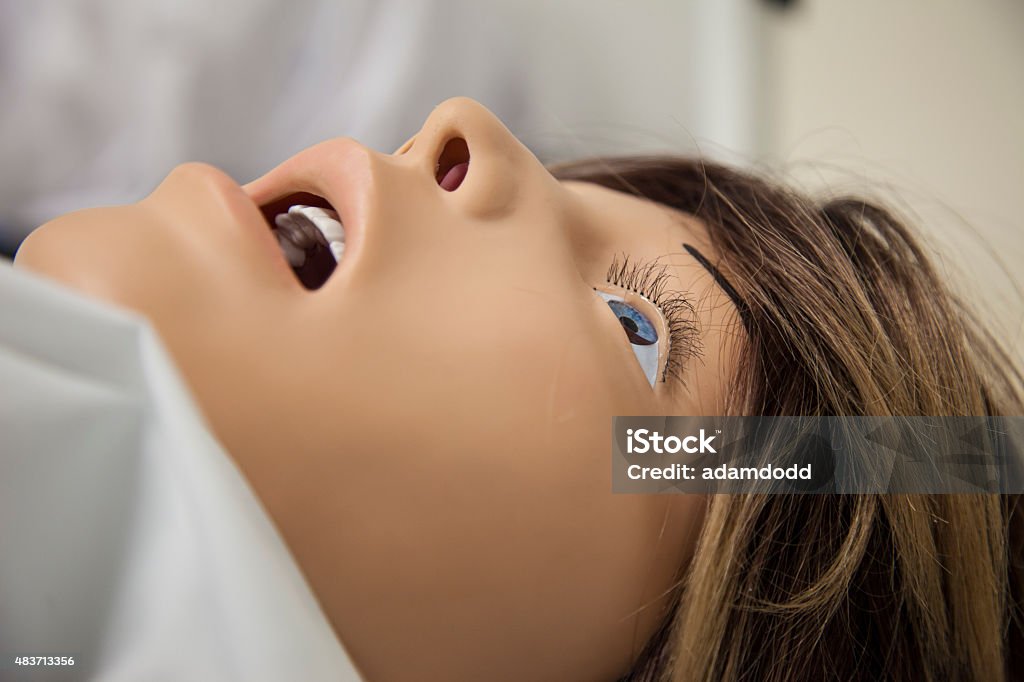 Hospital training dummy from side, close up, profile A hospital training dummy lying in a training hospital bed wearing a white hospital gown. Horizontal image with the dummy filling most of frame and lots of white copy space around the dummy's head. CPR Dummy Stock Photo