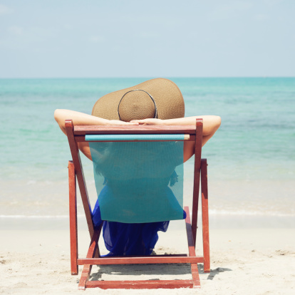 Woman relaxing on a tropical beach with hat. Outdoors