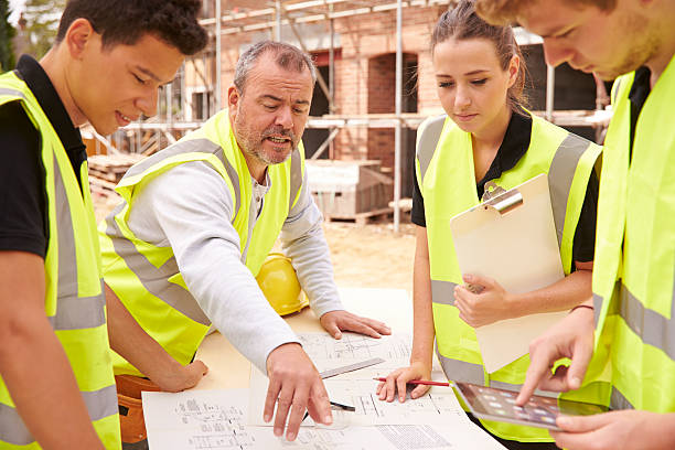 Builder On Building Site Discussing Work With Apprentice Builder On Building Site Discussing Work With Apprentice trainee stock pictures, royalty-free photos & images