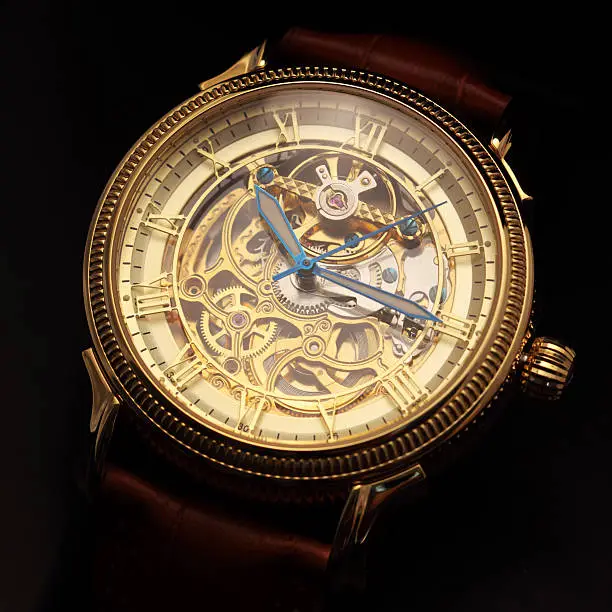 Golden wristwatch with a visible clockwork on black background.