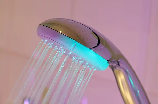 Image of a shower head with running water illuminated by a multi colored spotlight with pastel colors