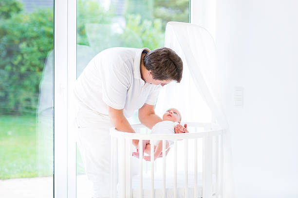 istock Smiling father tooking baby from round crib standing at window 483721035