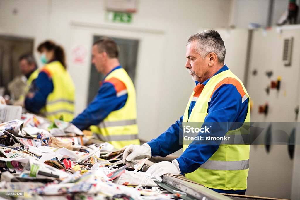 Senior man working at paper recycling plant Senior worker sorting papers on factory assembly line for recycling at recycling plant. Recycling Stock Photo