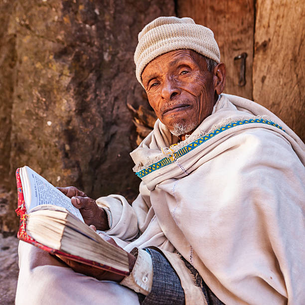 monk leggendo il libro di preghiera vicino a una delle chiese di lalibela - travel ethiopia foto e immagini stock