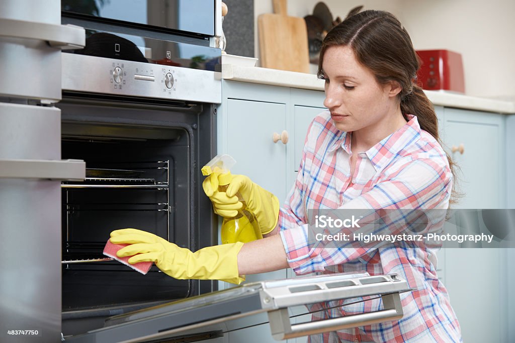 Fed Up Woman Cleaning Oven At Home 2015 Stock Photo