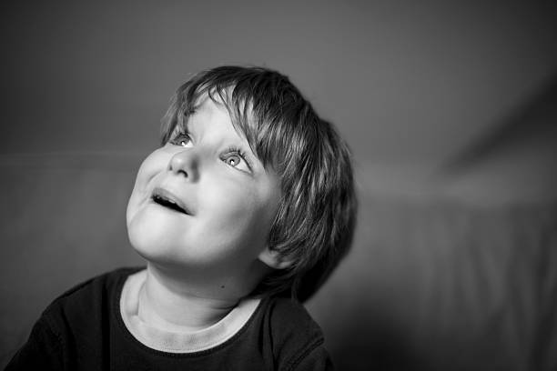 A close up portrait of a baby boy looking up. Processed in black and white. Some copy space in black background.