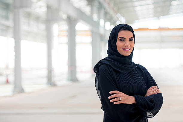 Confident Emirati Businesswoman Confident arab businesswoman standing in a new hall, built for her business. She is looking proudly into the camera, smiling. She have her arms crossed. united arab emirates stock pictures, royalty-free photos & images