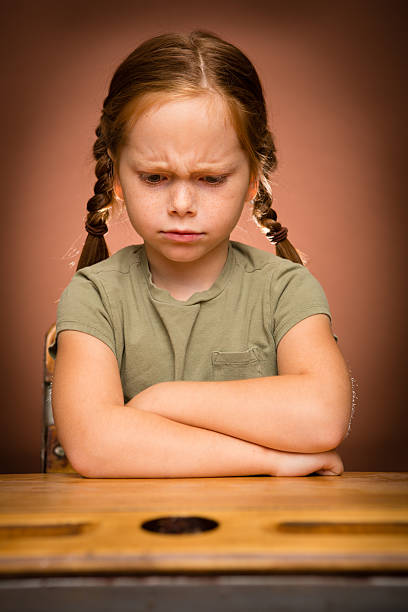 недоволен молодая девушка студент, сидя на школе стол - anger child braids braided стоковые фото и изображения